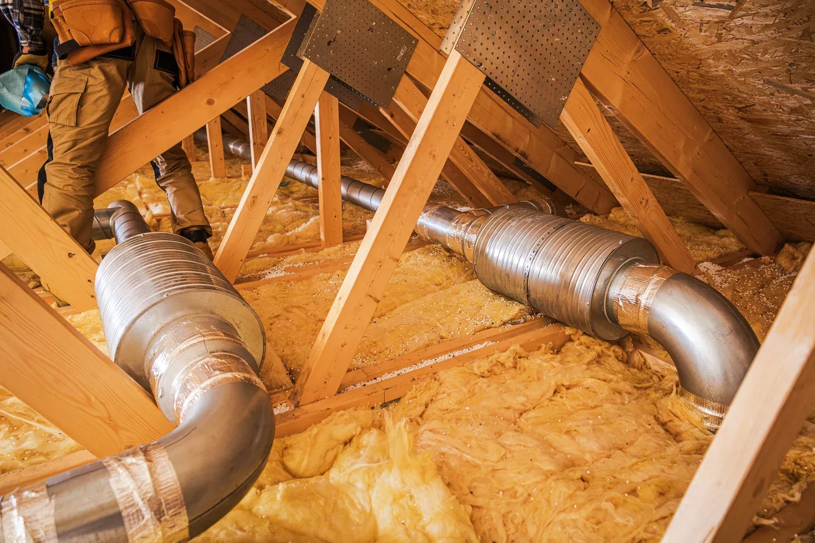 HVAC ducts snaking through attic rafters, surrounded by insulation.