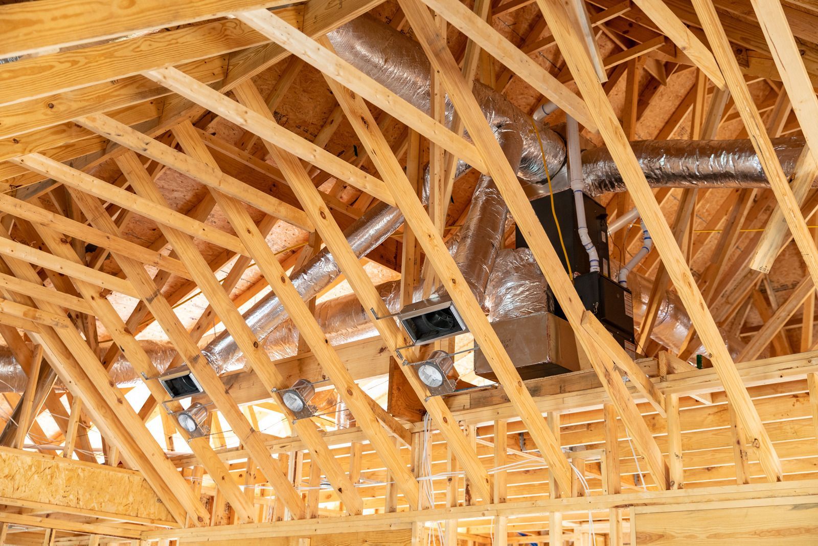 Wooden roof framing with HVAC ductwork and vents installed.