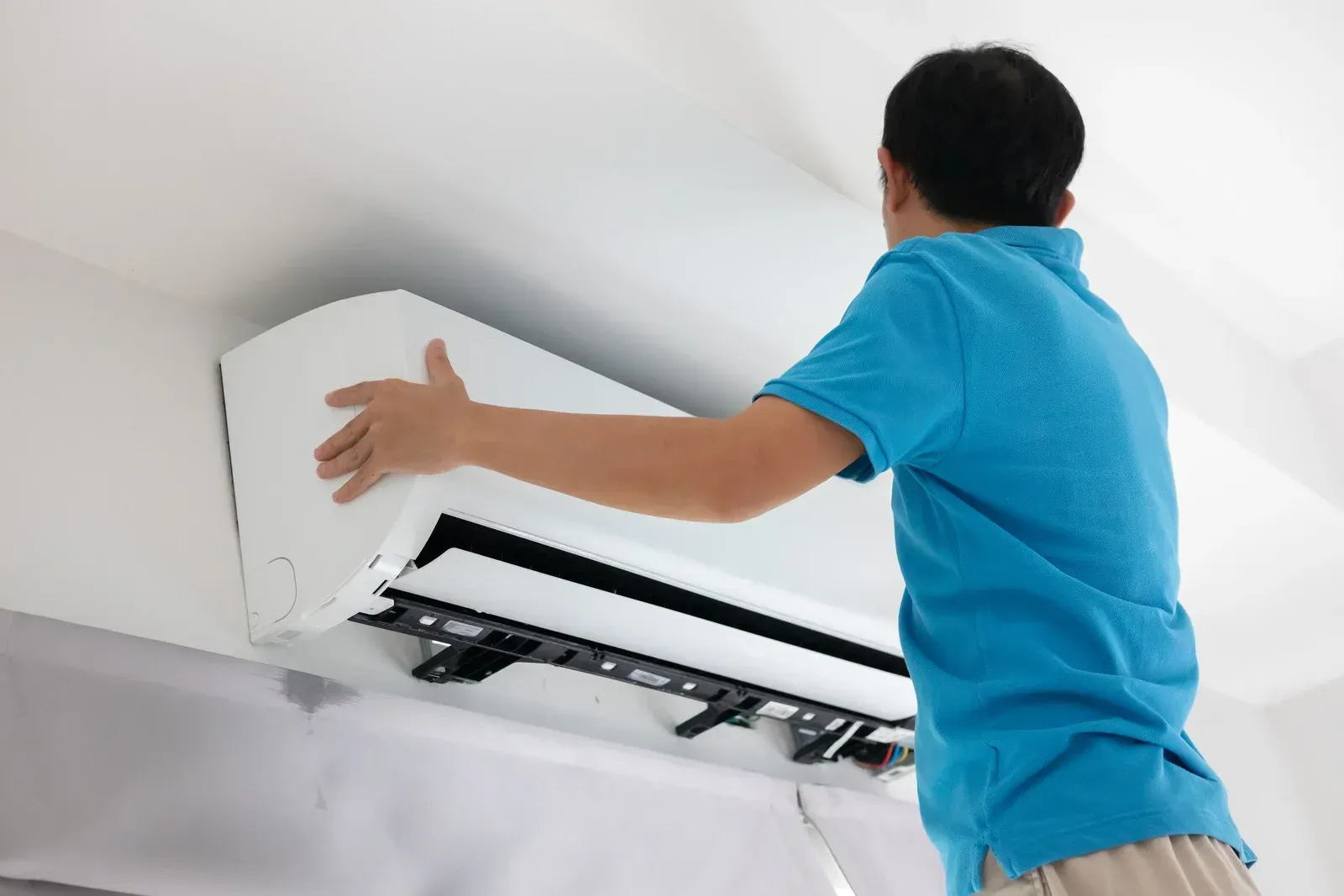 Person in blue shirt touching a white air conditioning unit mounted on a wall.