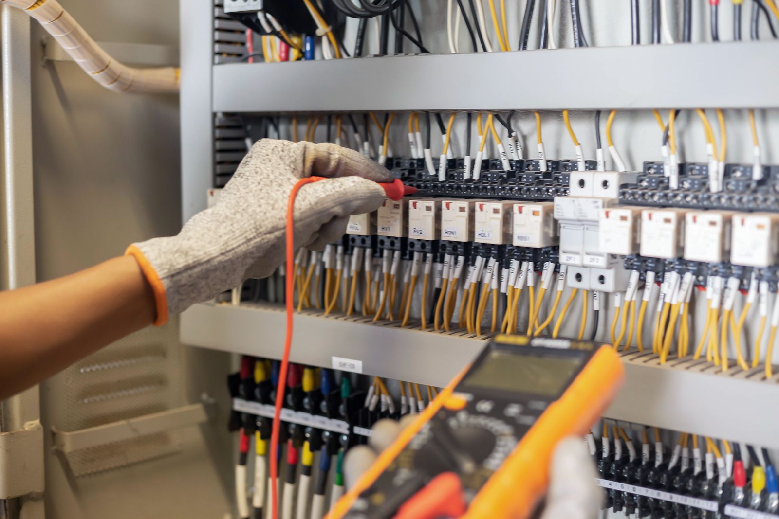Electrician tests wiring with multimeter in control panel.