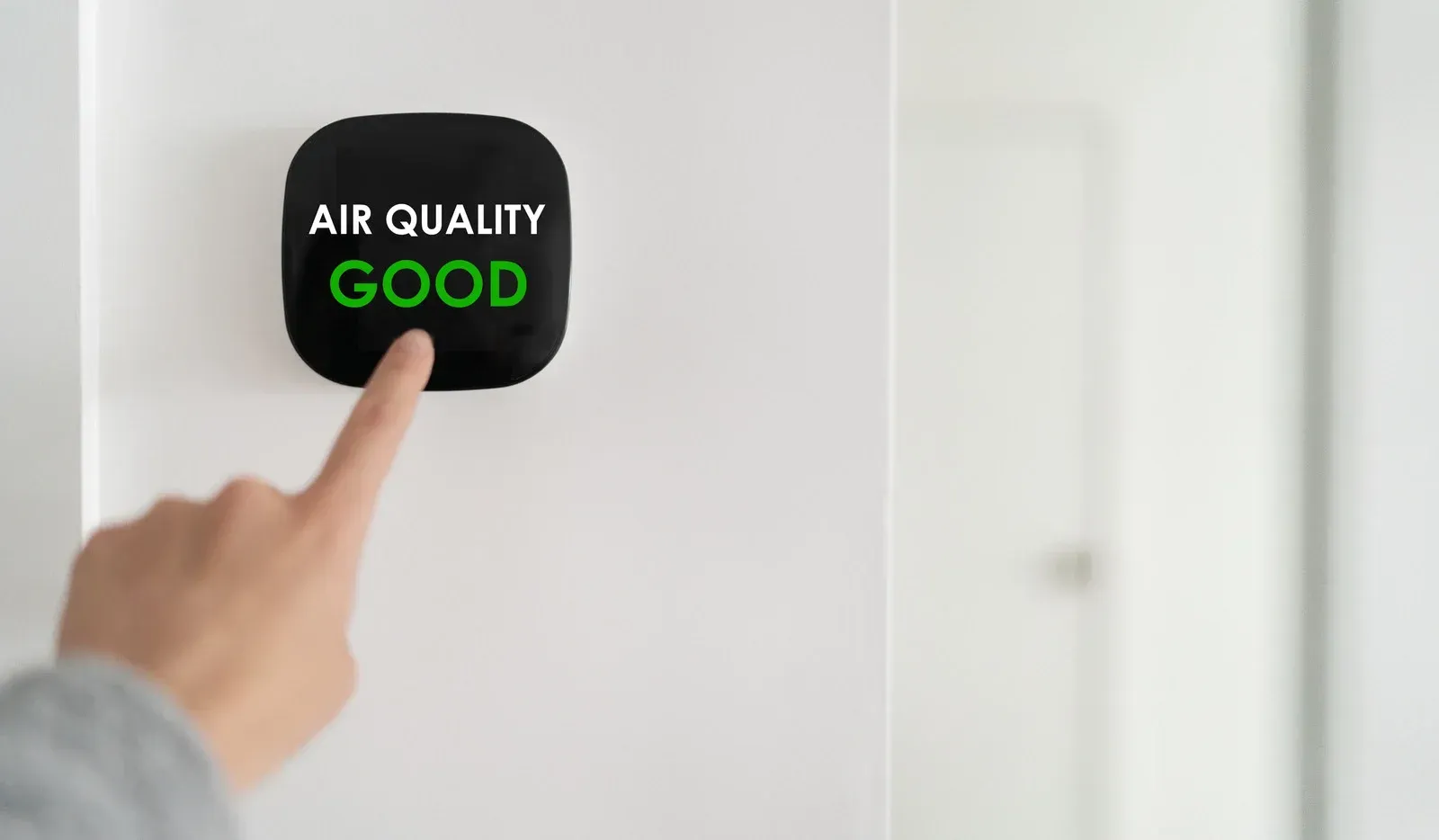 Hand pointing at an air quality monitor displaying 