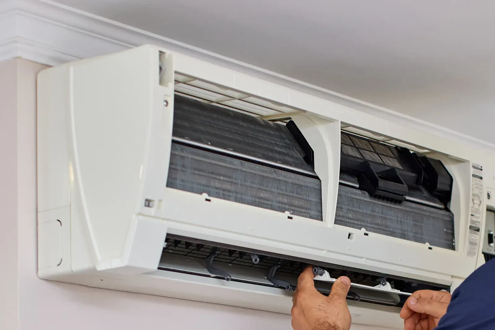 Person cleaning an air conditioning unit mounted on a wall.