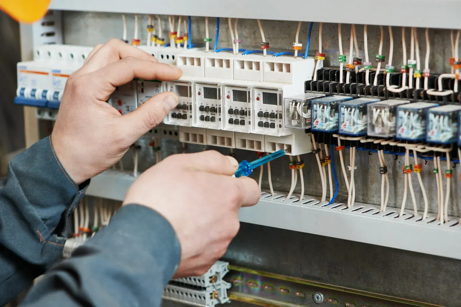 Electrician working on a control panel, using a screwdriver to adjust wiring.