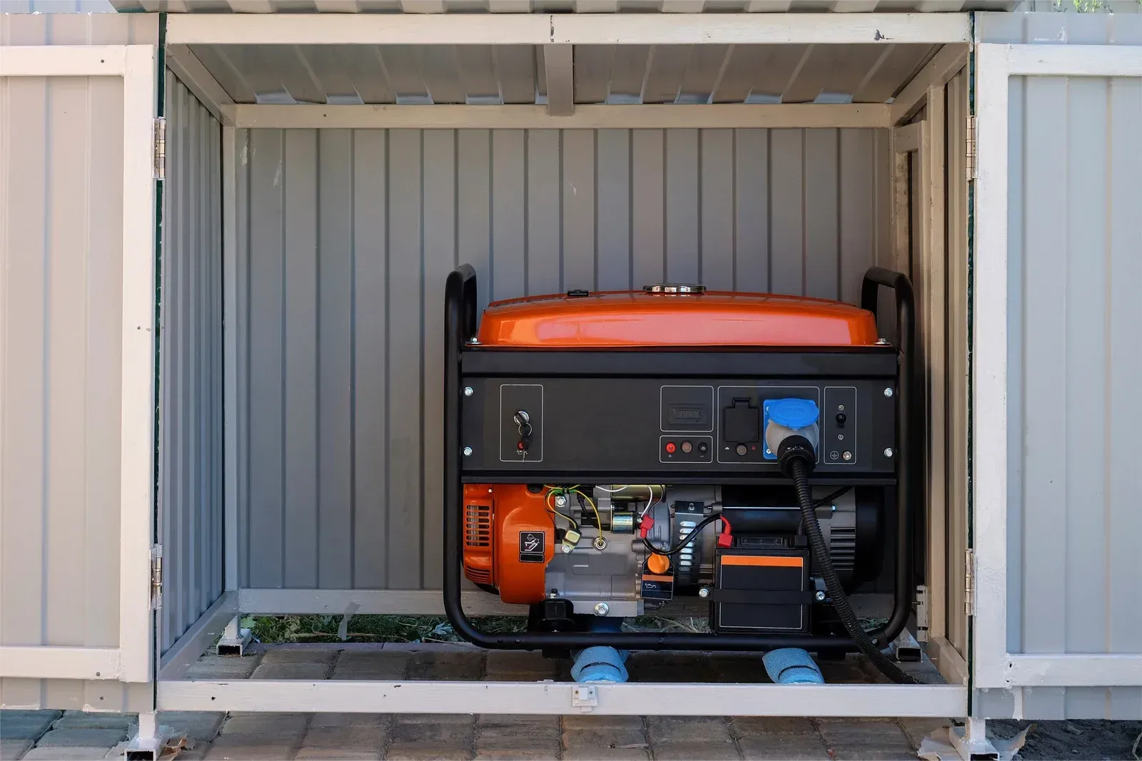 Generator inside a gray enclosure; orange and black colors; open doors.