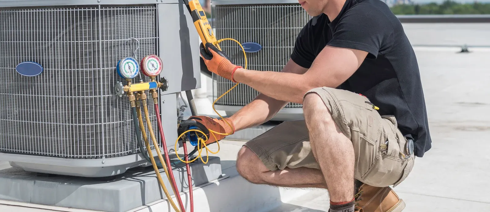 HVAC technician repairing an air conditioning unit on a rooftop, using gauges and tools.