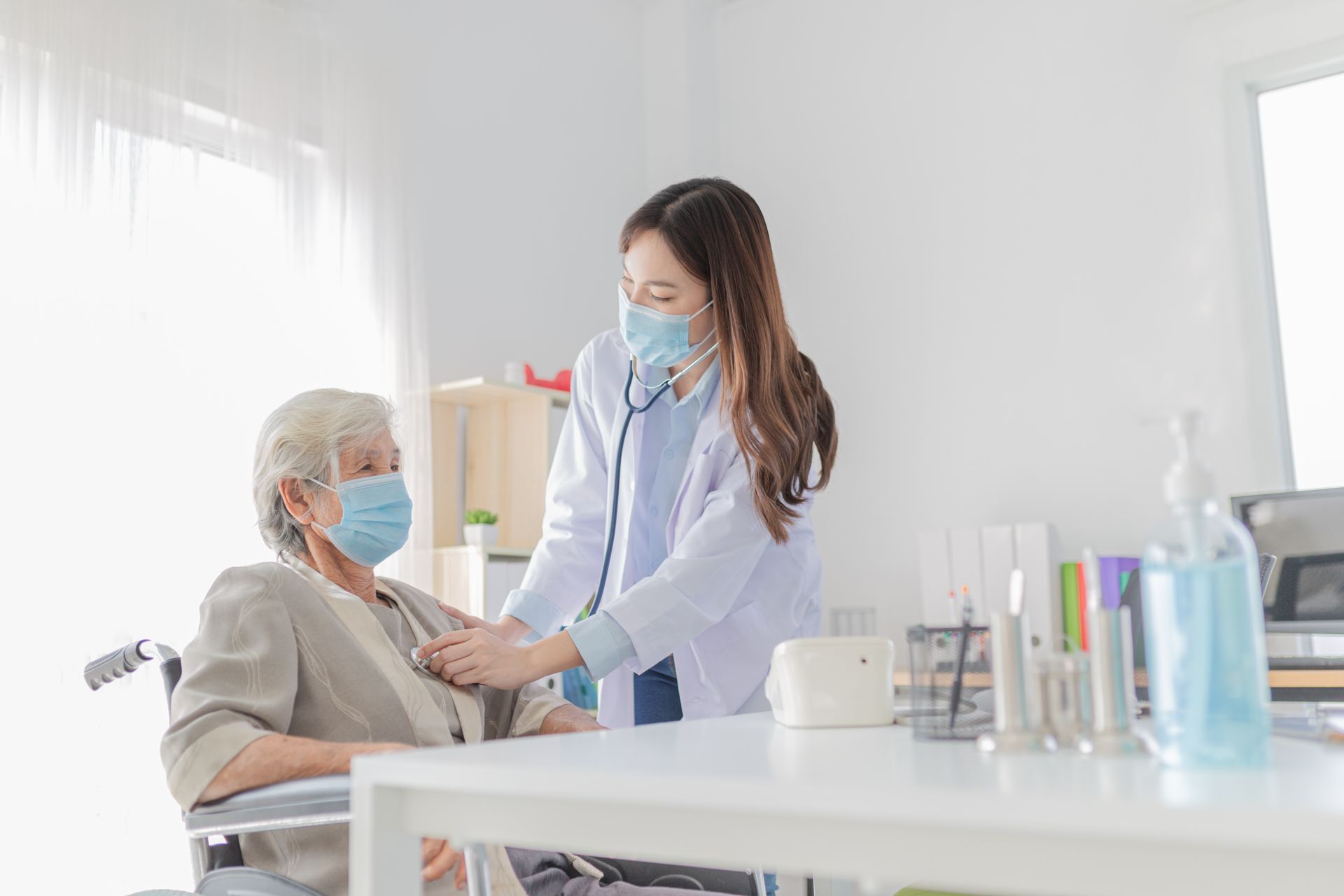 A nurse is examining an elderly woman in a wheelchair with a stethoscope.
