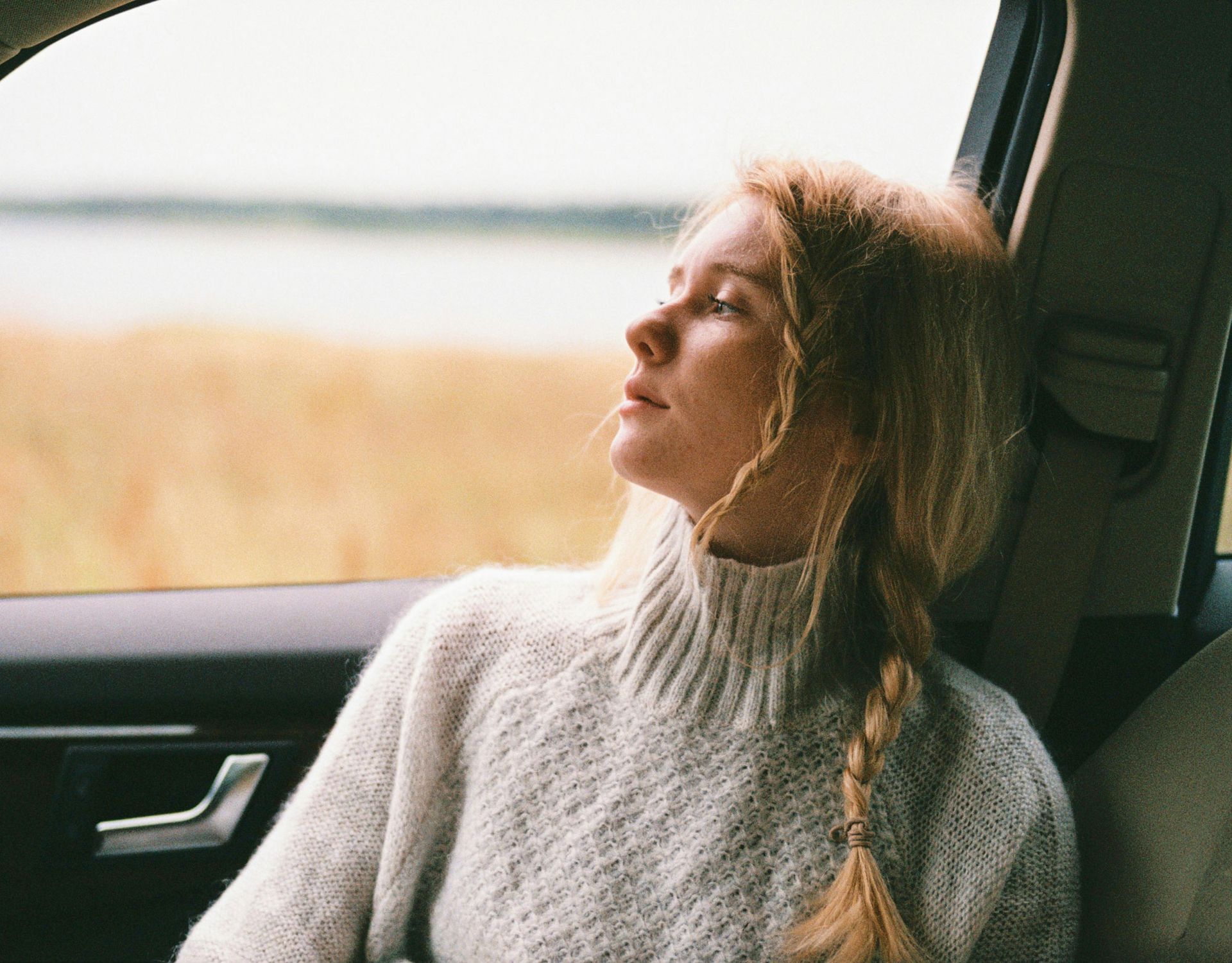 A woman in a sweater is sitting in the back seat of a car looking out the window.