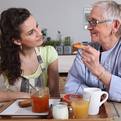 Pflege- und Betreuungskraft beim gemeinsamen Frühstück mit einer älteren Dame.