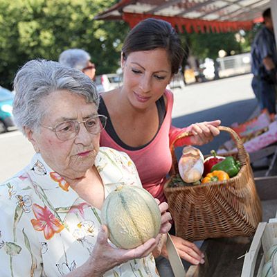 Ältere Frau gemeinsam mit Pflege- und Betreuungskraft beim Einkauf auf dem Markt.