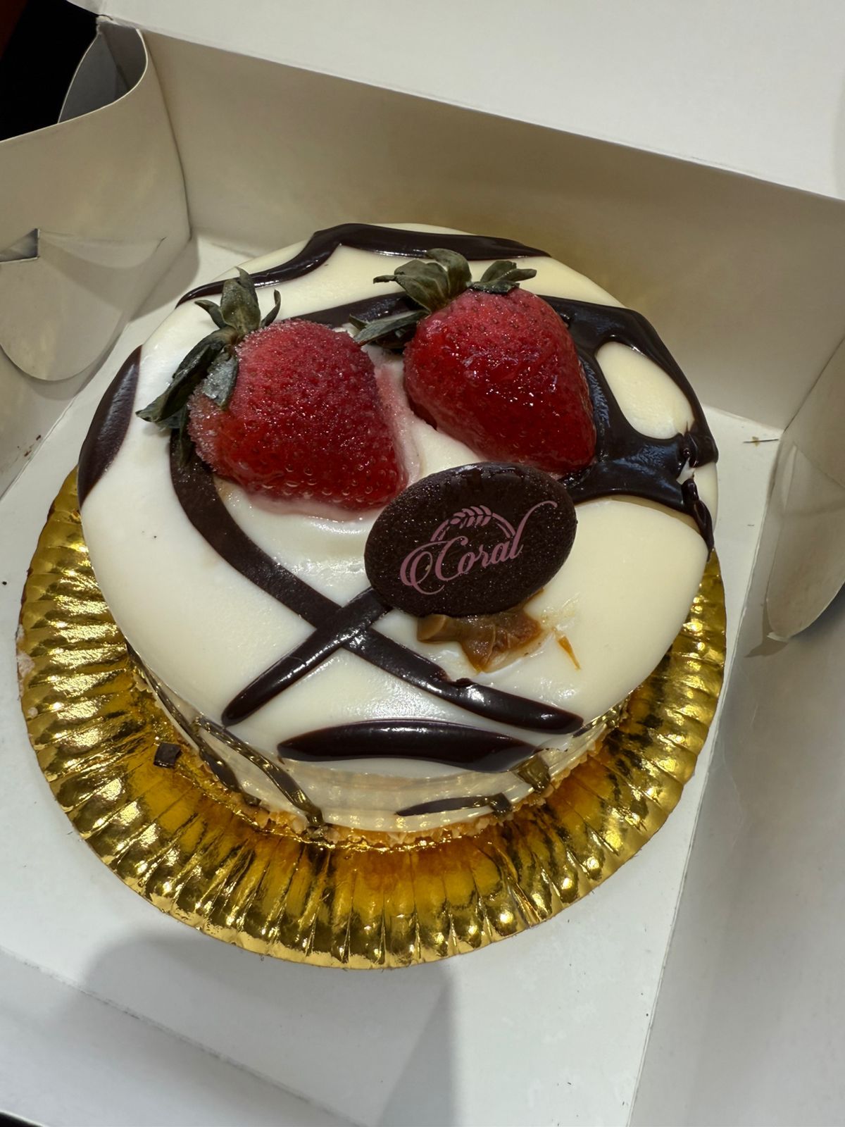 Pequeño pastel blanco con fresas y llovizna de chocolate sobre un tapete de papel dorado.