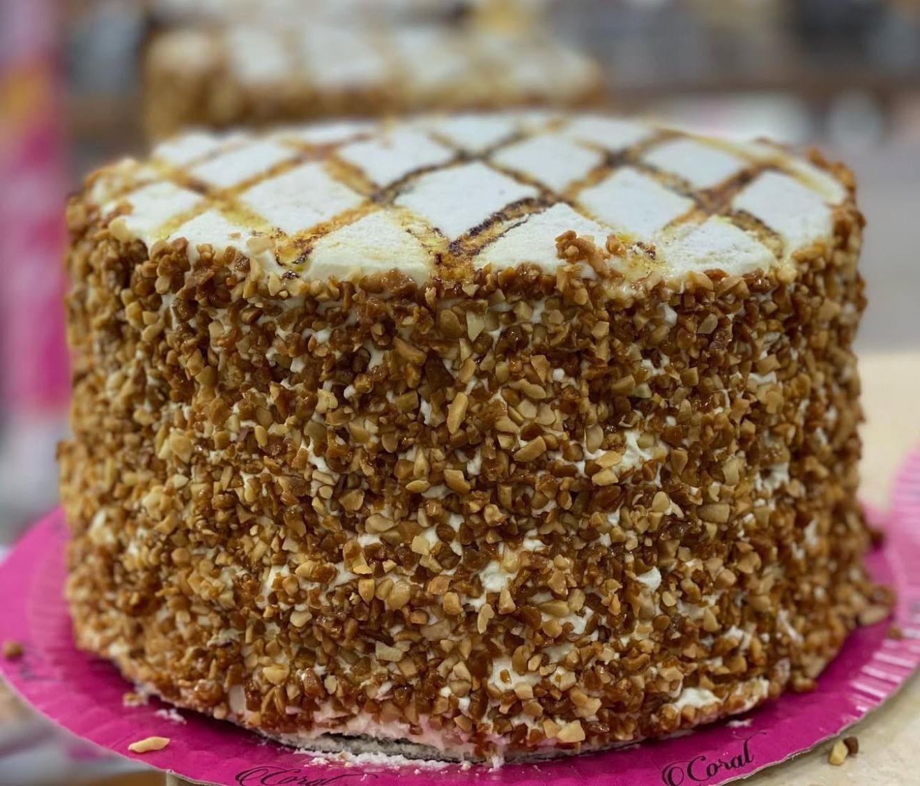 Pastel con lados cubiertos de nueces y una parte superior con diseño de diamantes, en un plato de papel rosa.