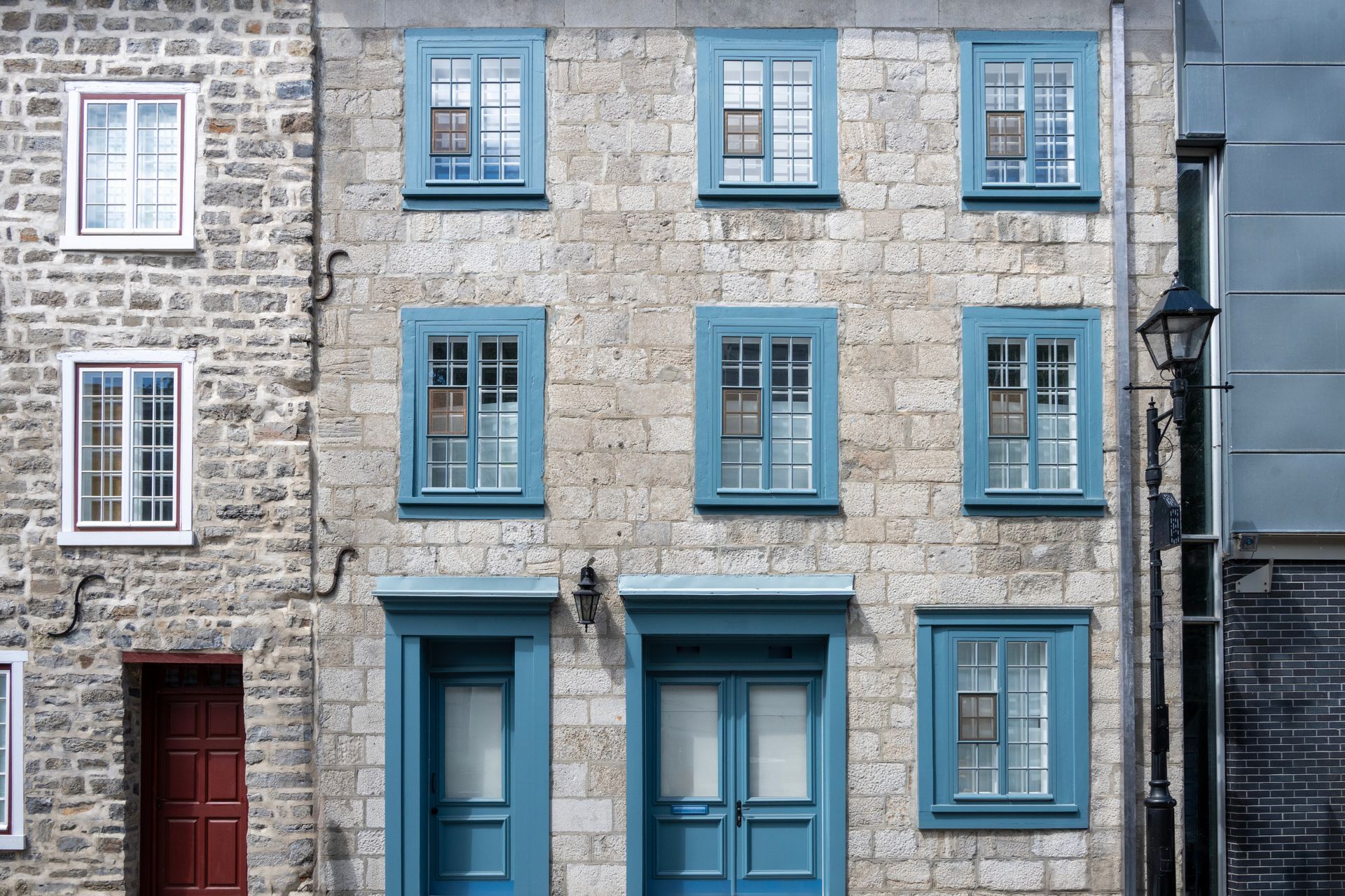 Bâtiment en pierre avec fenêtres et portes bleu sarcelle ; porte rouge à gauche.
