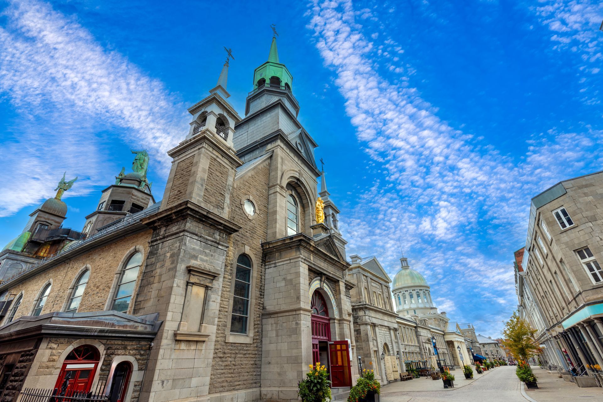 Église en pierre aux flèches vertes sous un ciel bleu, avec une rue bordée de bâtiments.