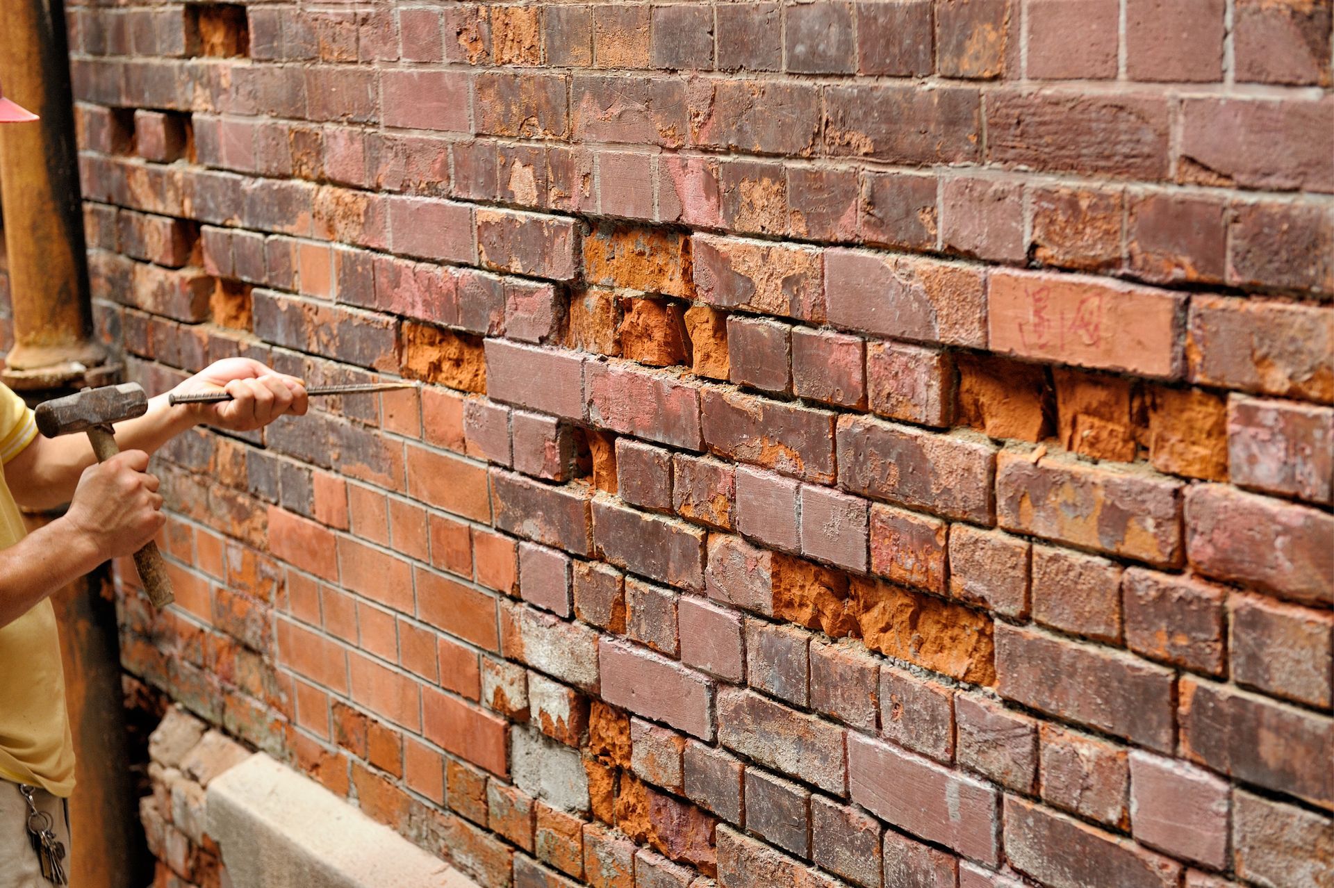 Mur de briques avec des dommages importants, ouvrier le répare avec des outils.