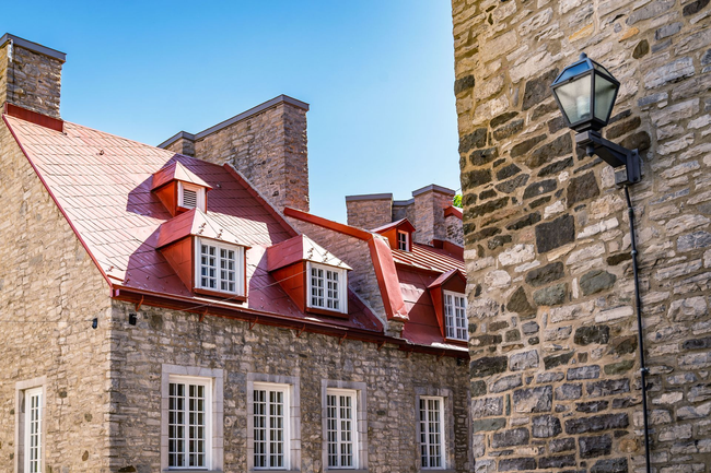 Bâtiments en pierre aux toits rouges et aux fenêtres à cadre blanc ; un vieux lampadaire sur un mur de briques.