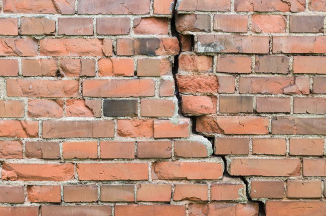 Mur de briques fissuré avec une grande fissure verticale; briques orange et brunes.