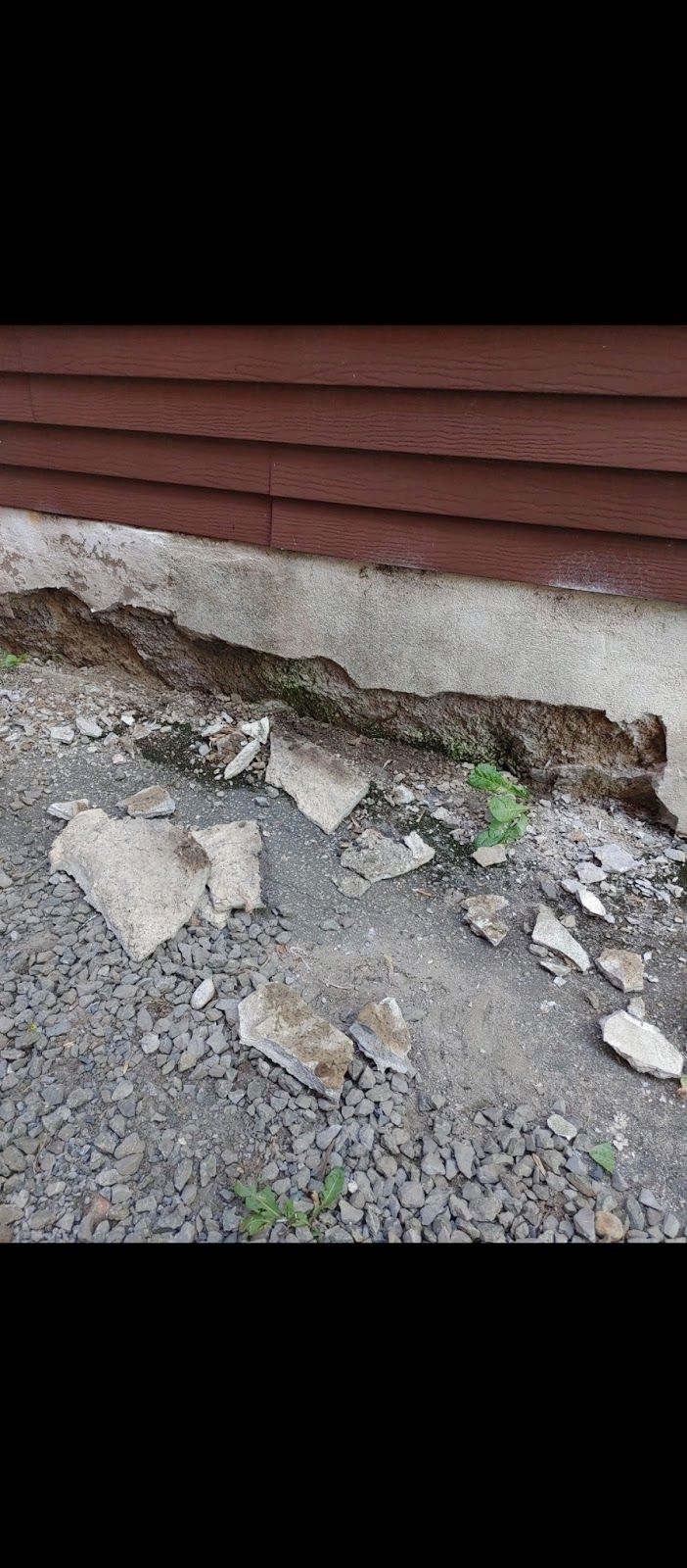 Gros plan sur du béton brisé et du gravier près des fondations d'un bâtiment en bois.