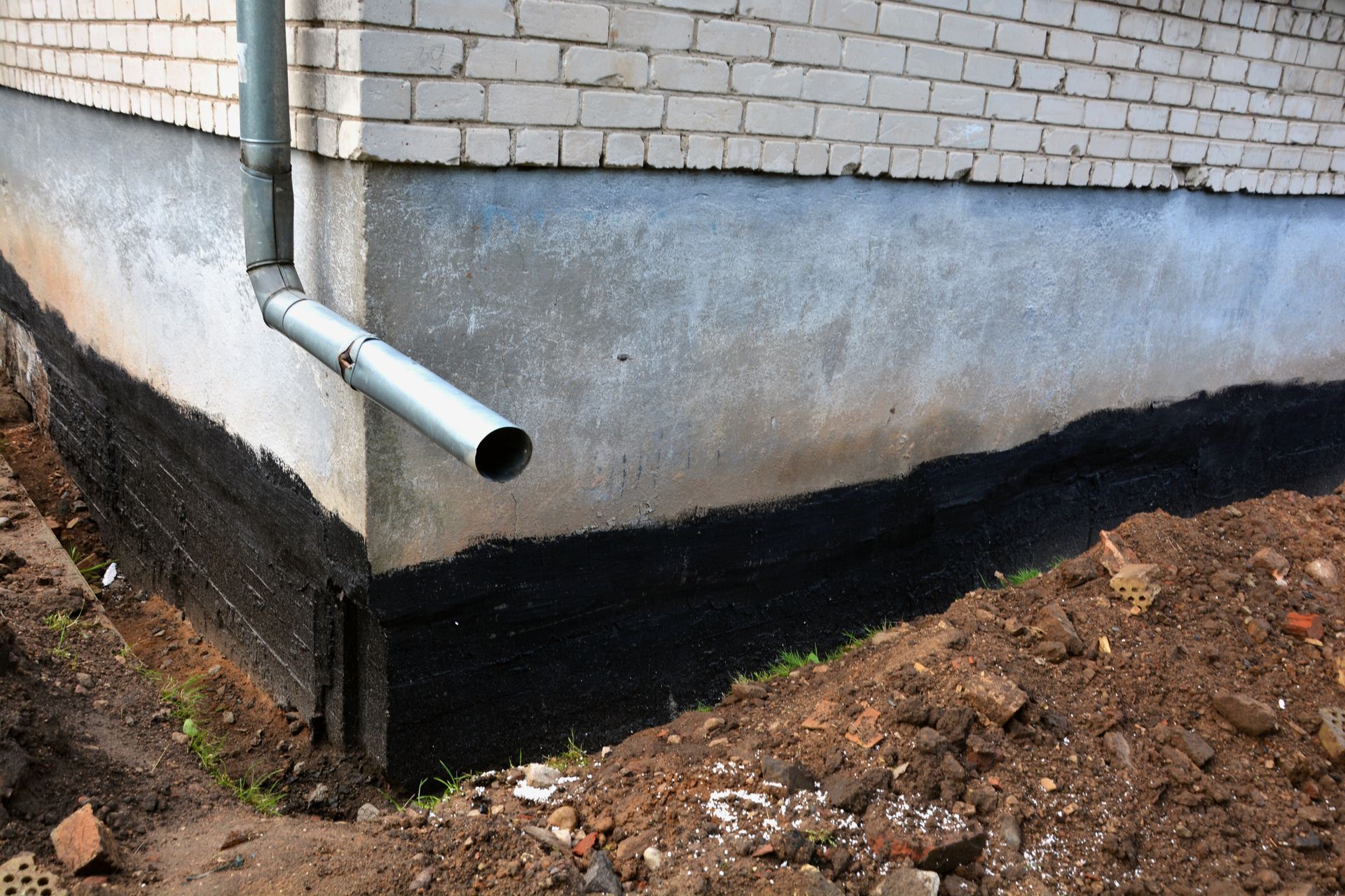 Fondation excavée d'un bâtiment en briques, avec barrière en plastique noir et sol sablonneux.
