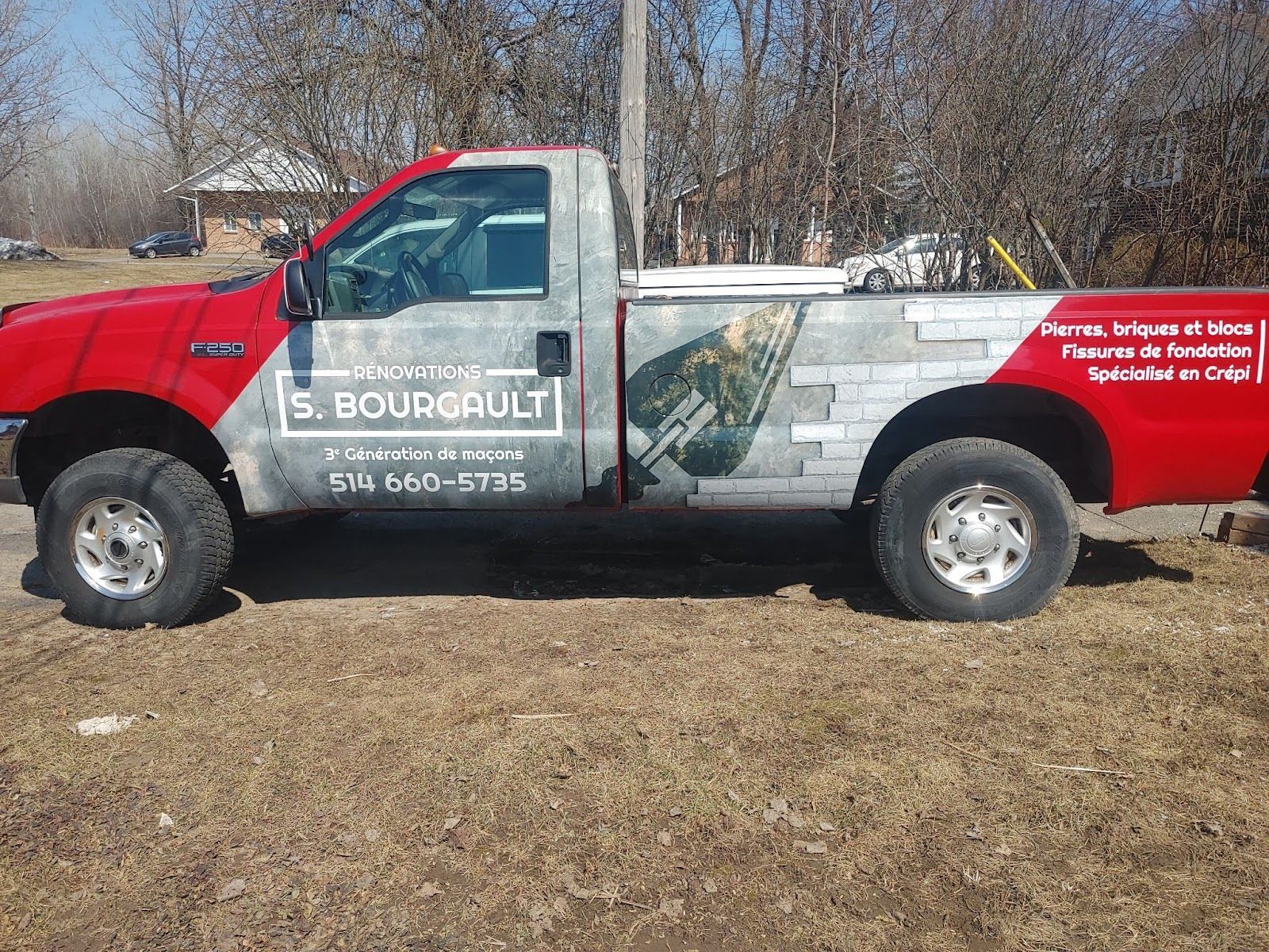 Camion de travail rouge et gris S. Bourgault stationné sur un bord herbeux; logo de l'entreprise visible.