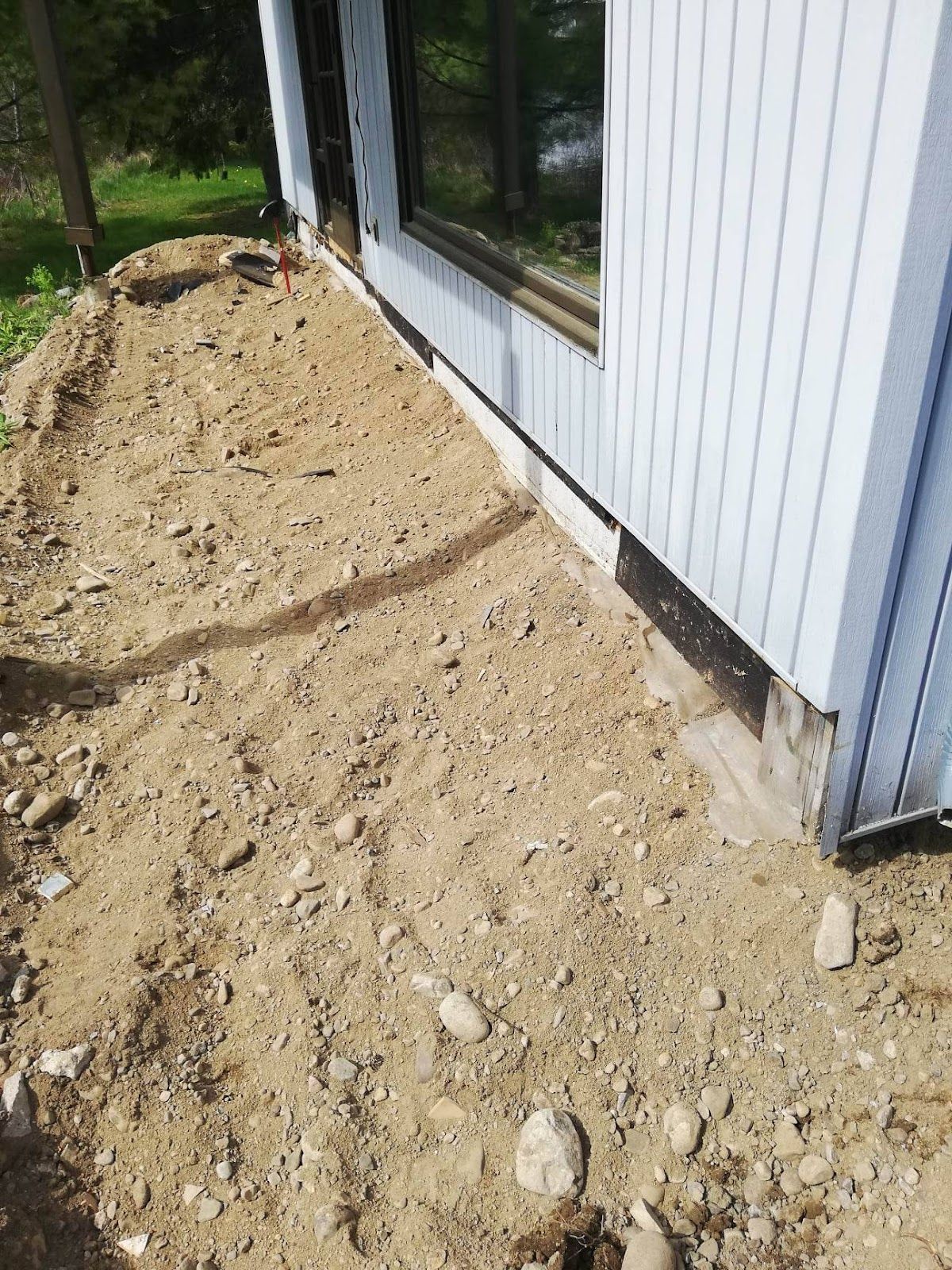 Tas de terre à côté d'un bâtiment avec un revêtement bleu et une fenêtre.