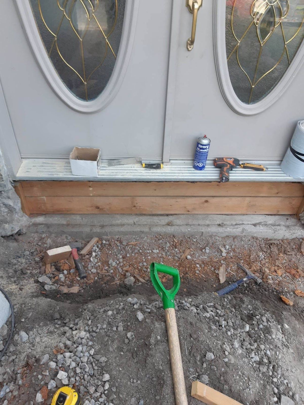 Personne construisant une petite marche en bois devant une porte, avec des outils et des matériaux éparpillés à proximité.