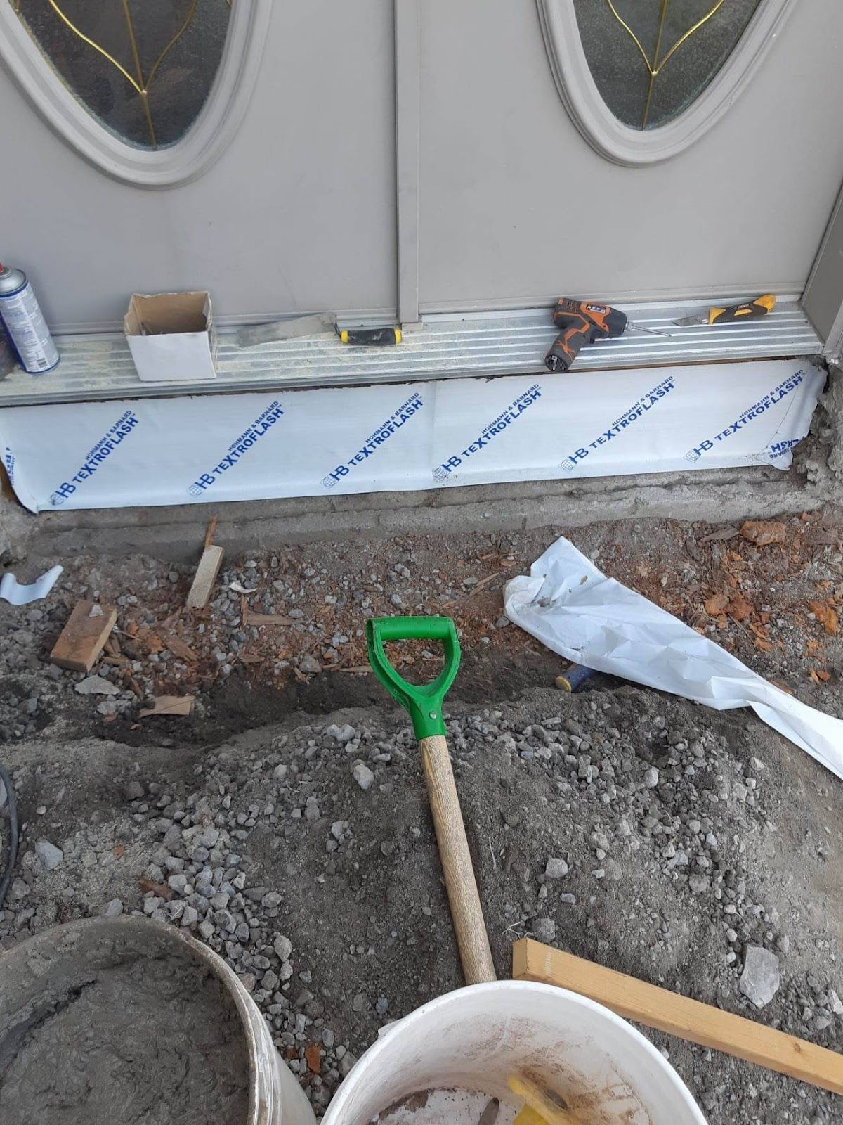 Chantier : seuil de porte en cours de réparation, pelle et seau à ciment visibles.