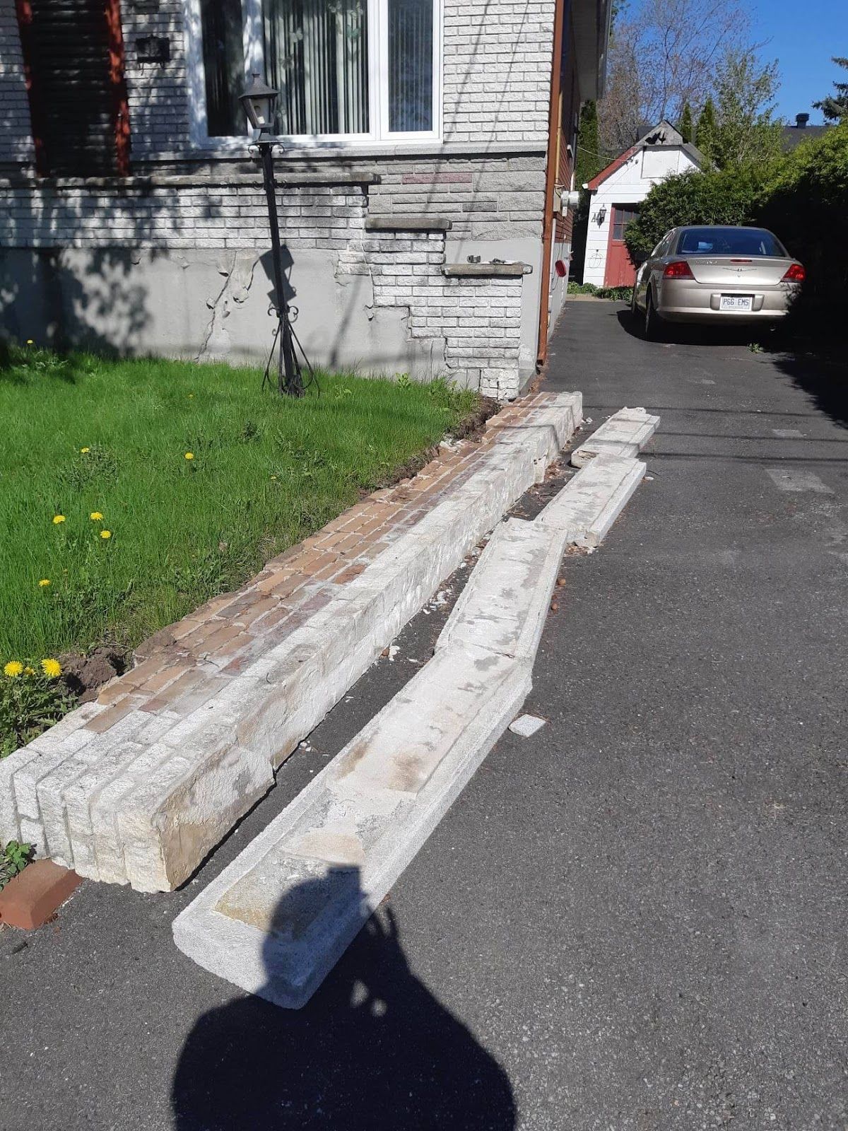 Des morceaux de béton brisés jonchent une allée près d'un bâtiment. Une voiture est garée à l'arrière-plan.