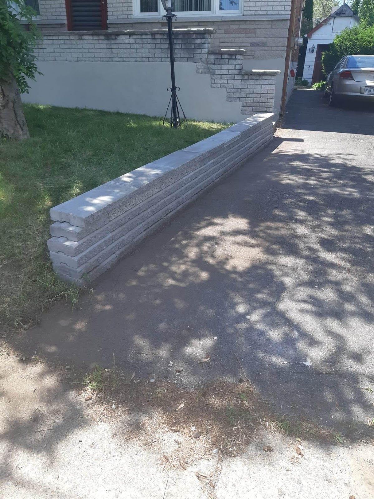 Pile de morceaux de bordure en béton gris sur une allée, près d'une maison et de l'herbe.