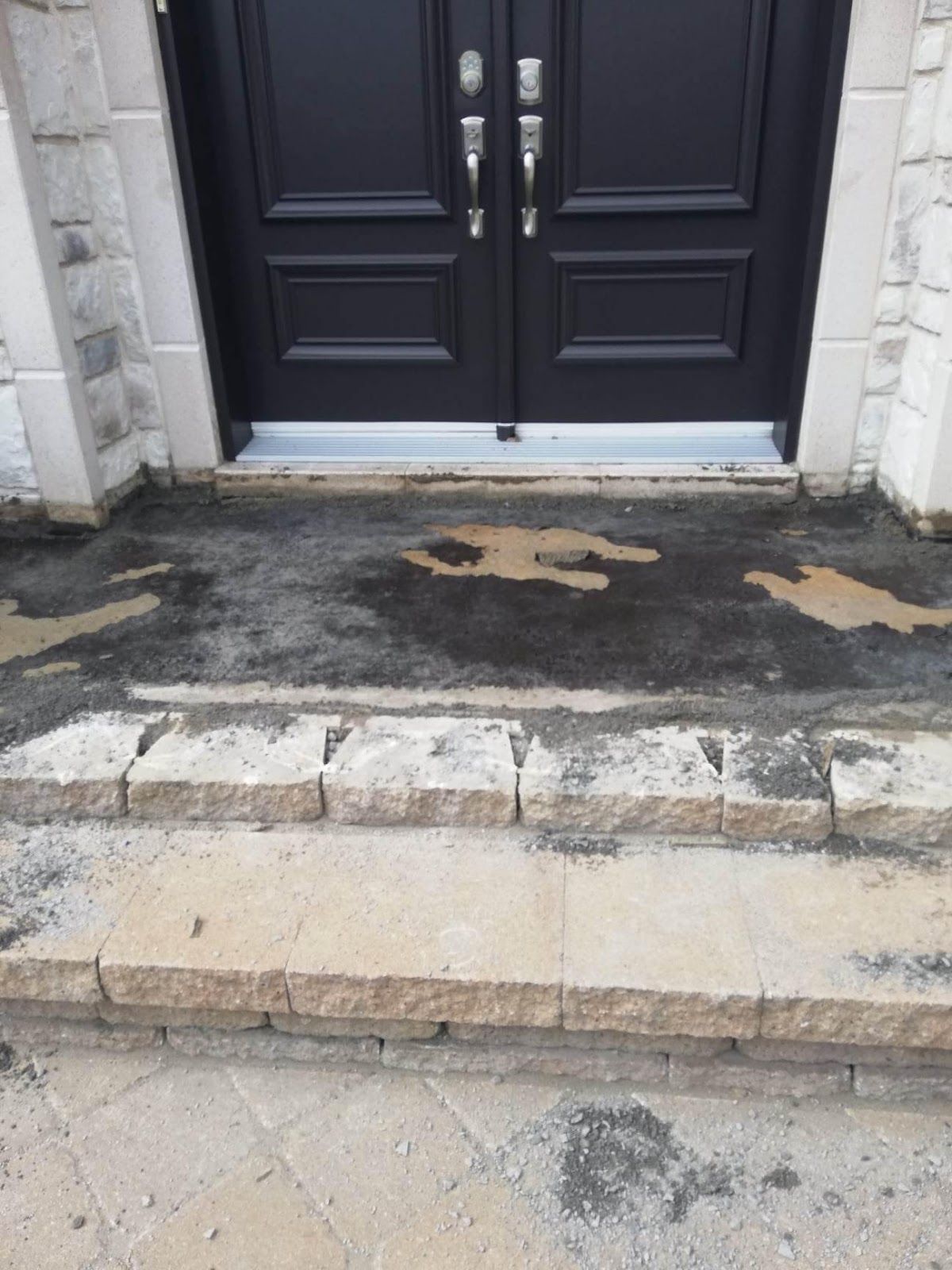 Marches en pierre menant à une entrée à double porte noire avec béton humide et garniture.