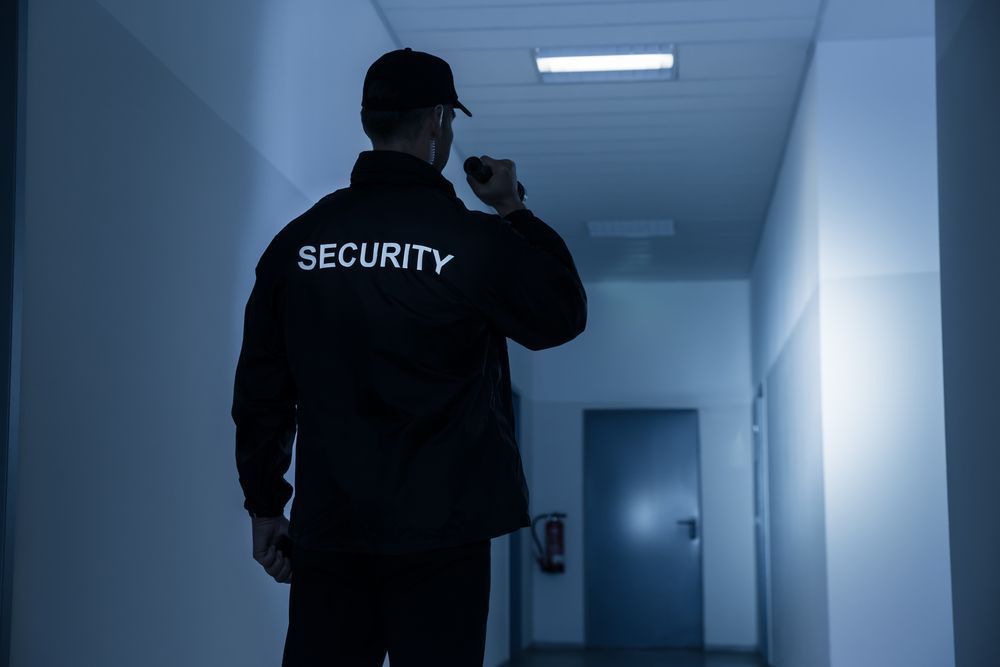 A Security Guard in Dark Uniform, Walking Down a Hallway, Holding a Radio — Clinton Security Services In Toowoomba, QLD