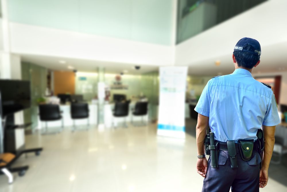 A Security Guard in Blue Uniform Stands in a Bank Lobby, Observing the Space — Clinton Security Services In Gold Coast, QLD