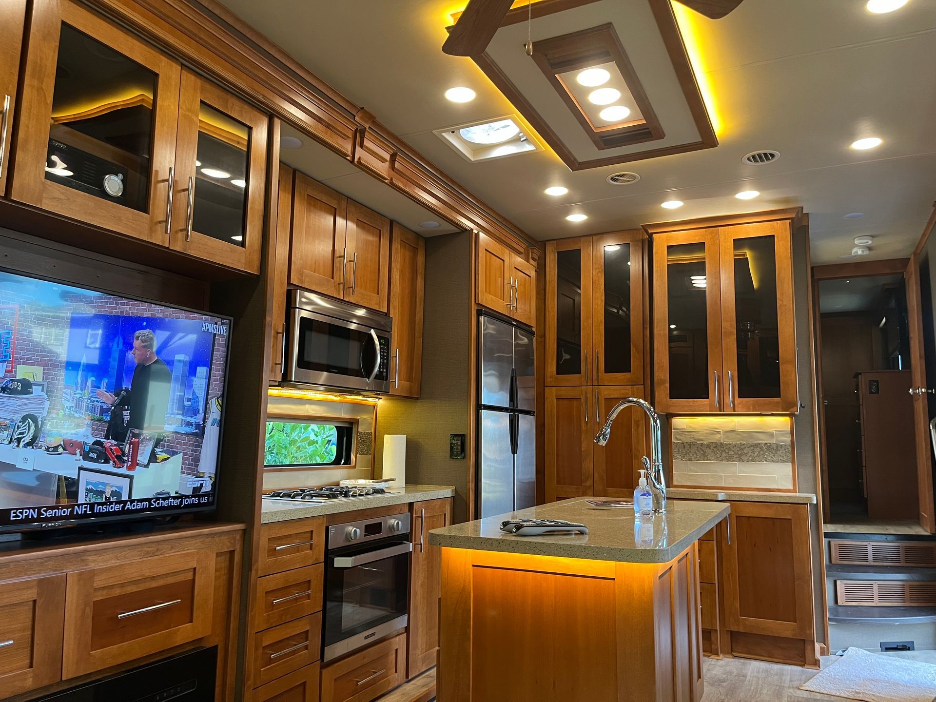 A kitchen with wooden cabinets , stainless steel appliances and a flat screen tv.