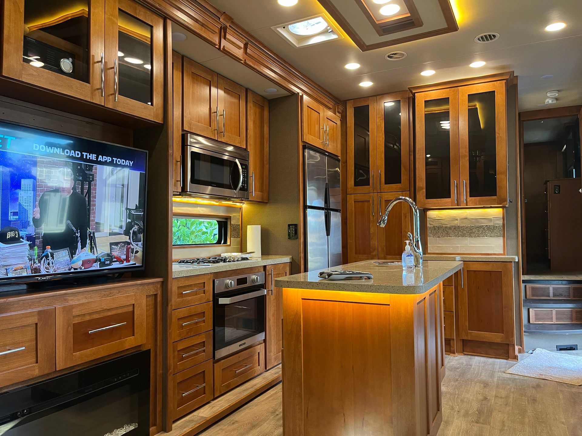 A kitchen in a rv with a large island and a flat screen tv.