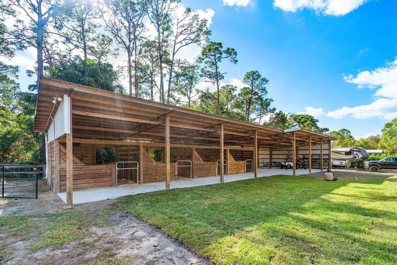 Two horses are standing under a covered area in a barn.