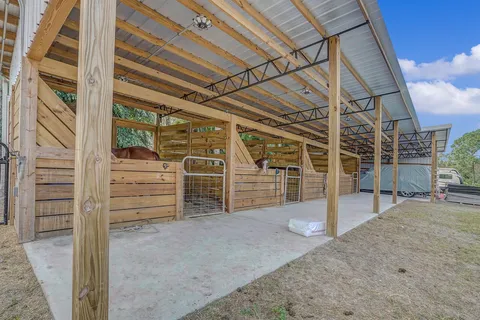 A horse stable with a metal roof and wooden fences.