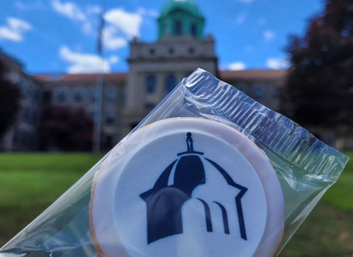 Cookie with building logo in front of a blurred building with a green dome and blue sky.