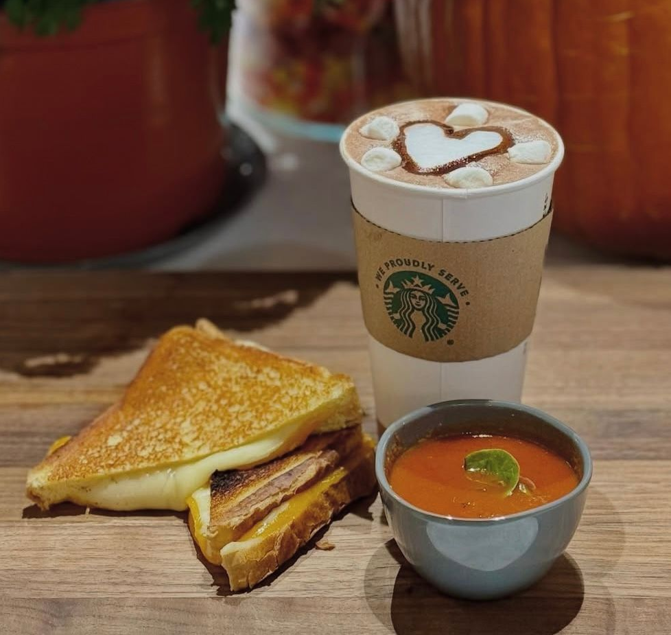 Grilled cheese sandwich, tomato soup, and Starbucks drink with marshmallow heart on wooden table.
