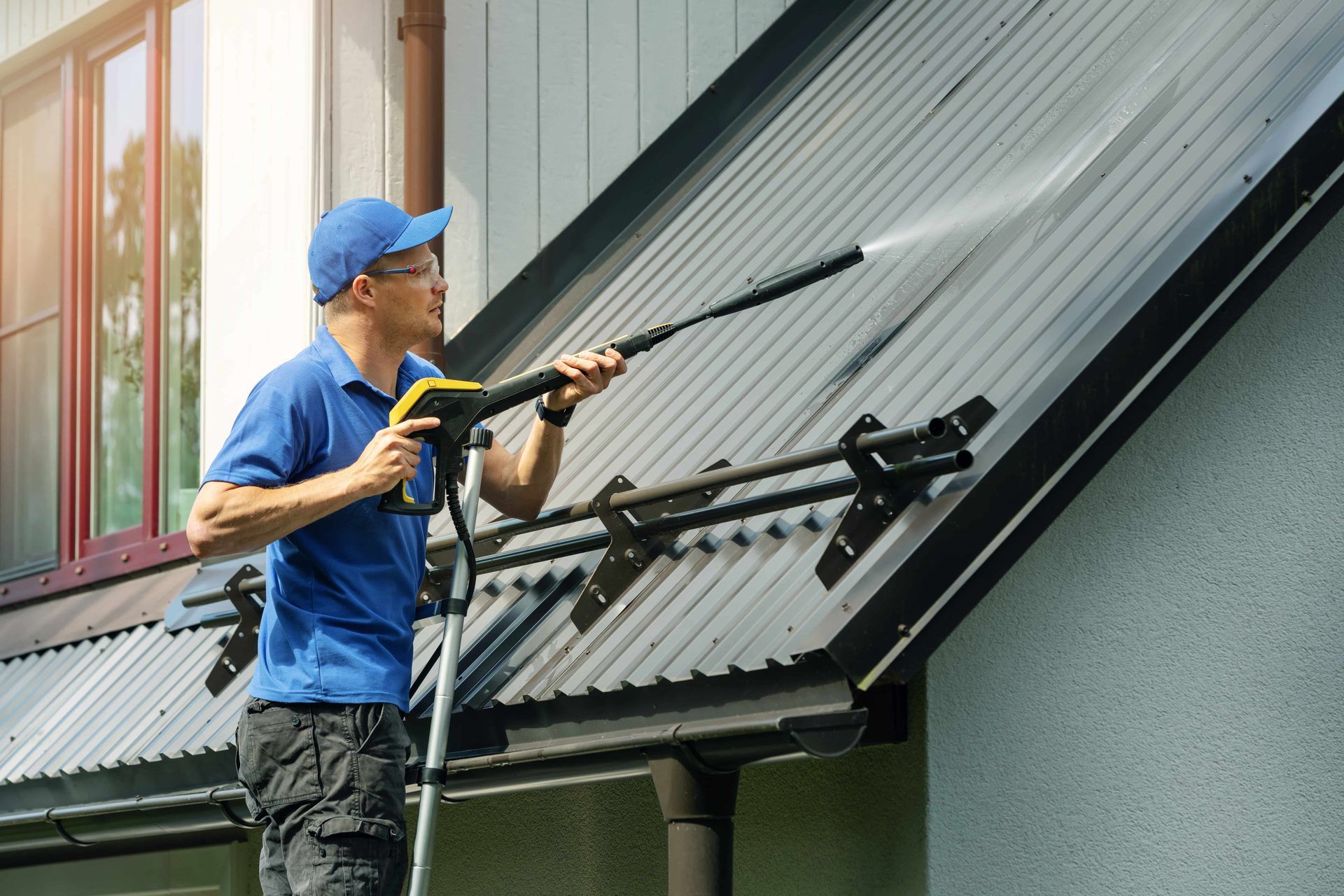Man in blue shirt power washing a metal roof.