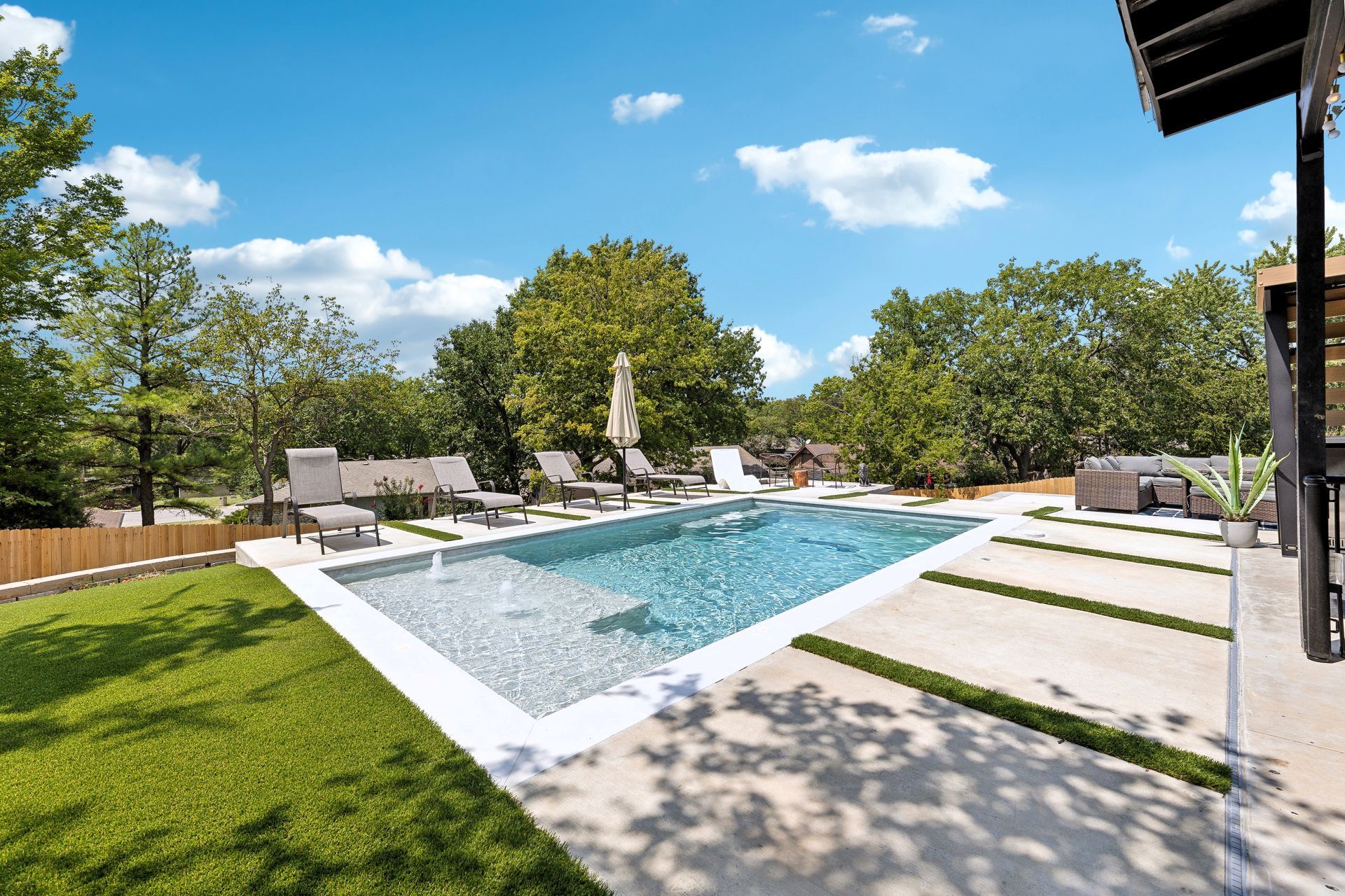 Pool and patio with lounge chairs and greenery on a sunny day.