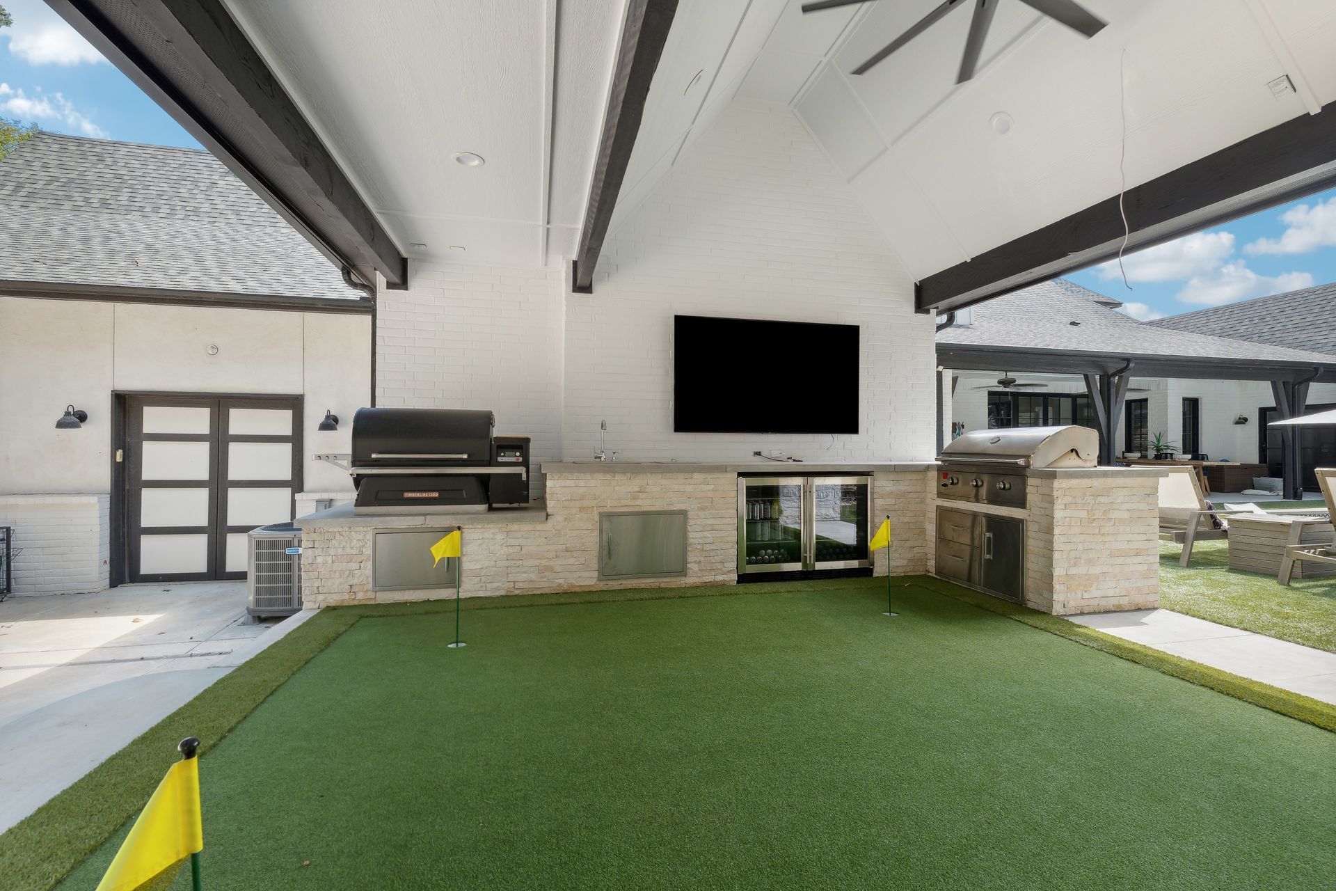 Outdoor entertainment space with a putting green, kitchen, and TV under a white roof.