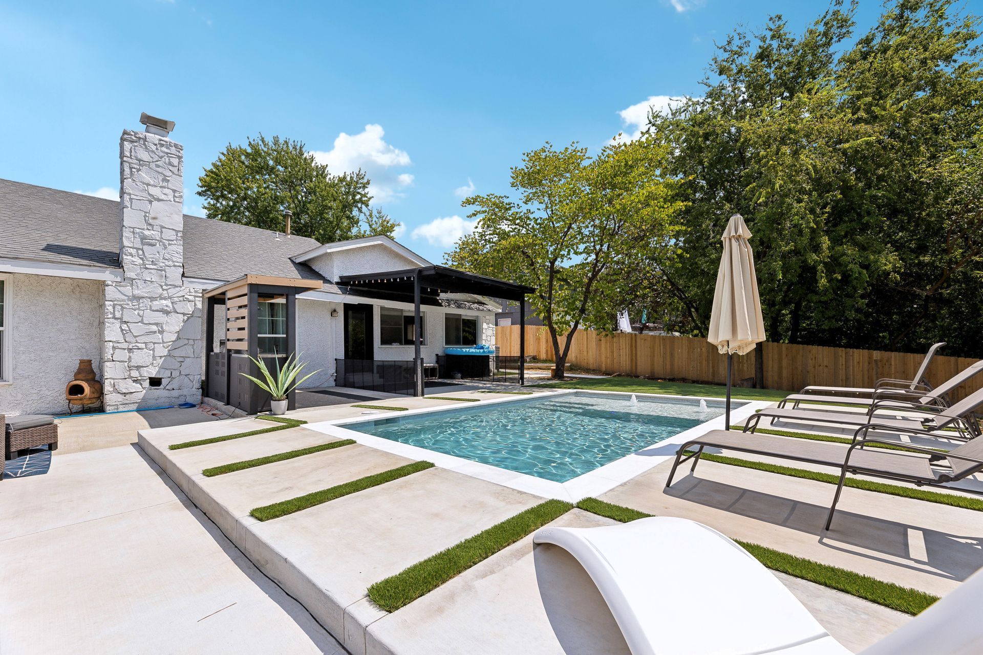 Backyard with pool, lounge chairs, pergola, and house; sunny day.
