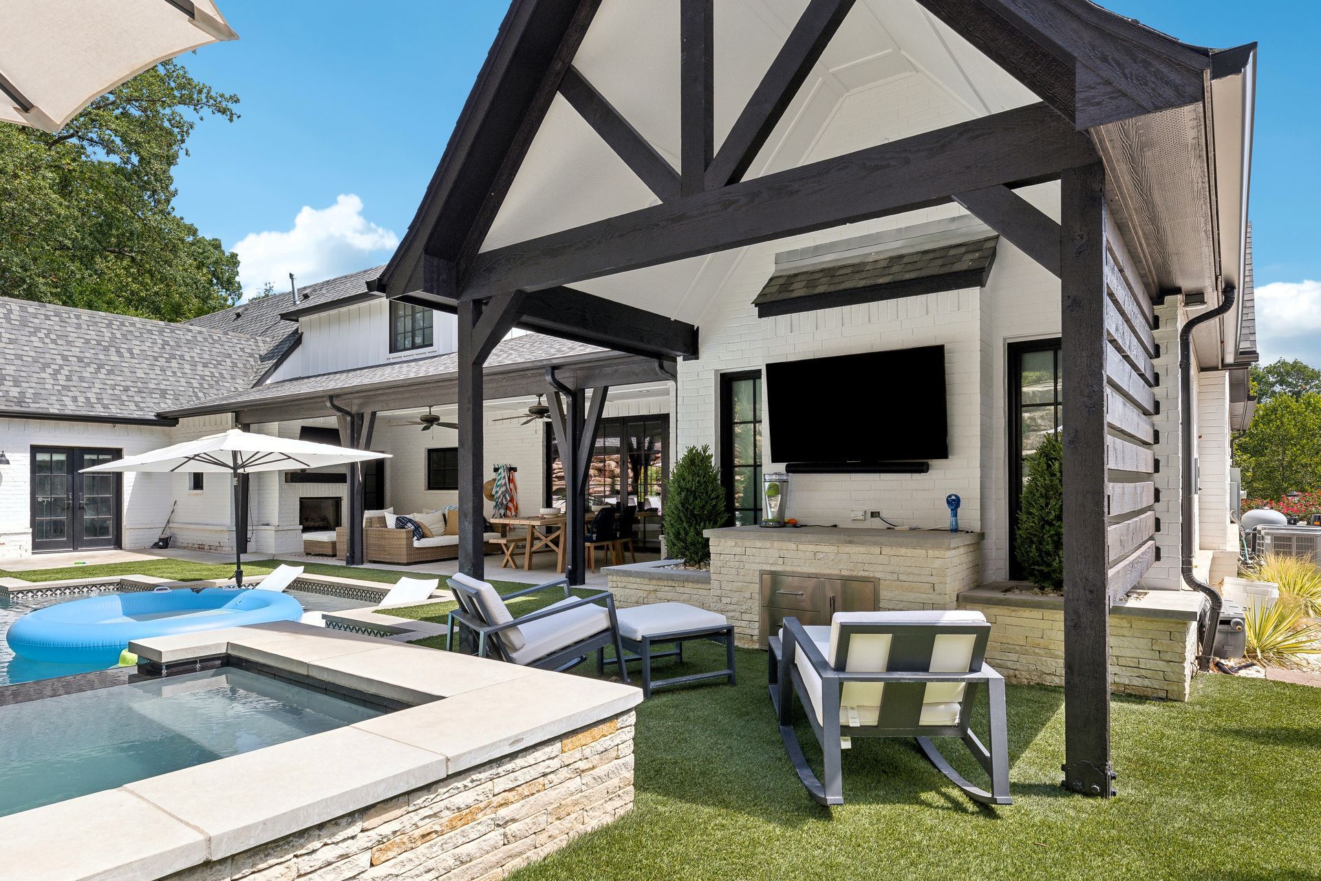 Backyard with pool, covered patio with TV, lounge chairs, and a white house.