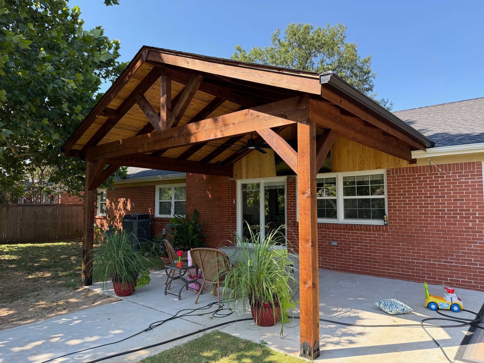 Pergola with woven roof over patio furniture, beside a house.