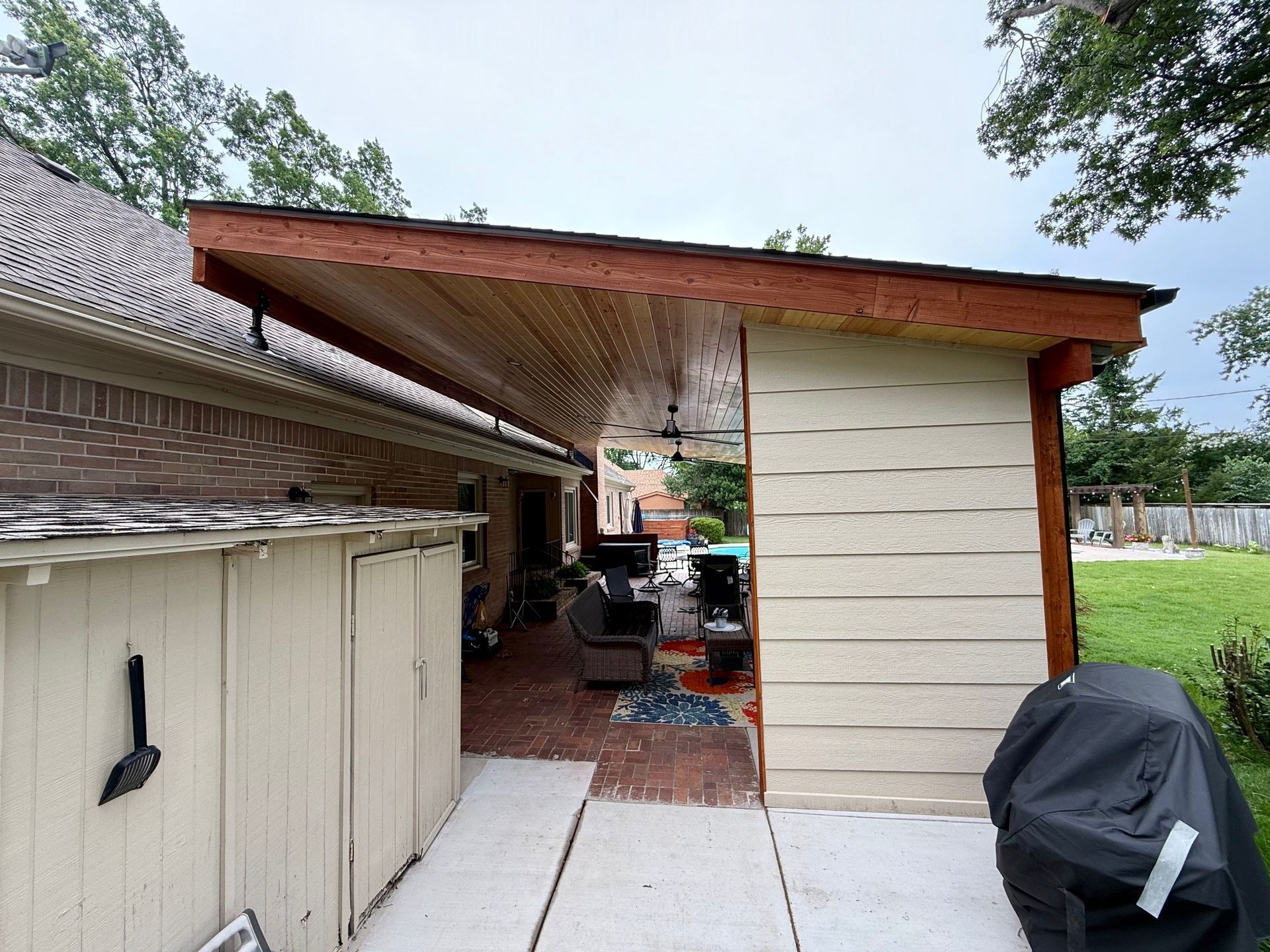 Backyard patio with pergola, pool, and house. Wooden structure, outdoor furniture, blue water.