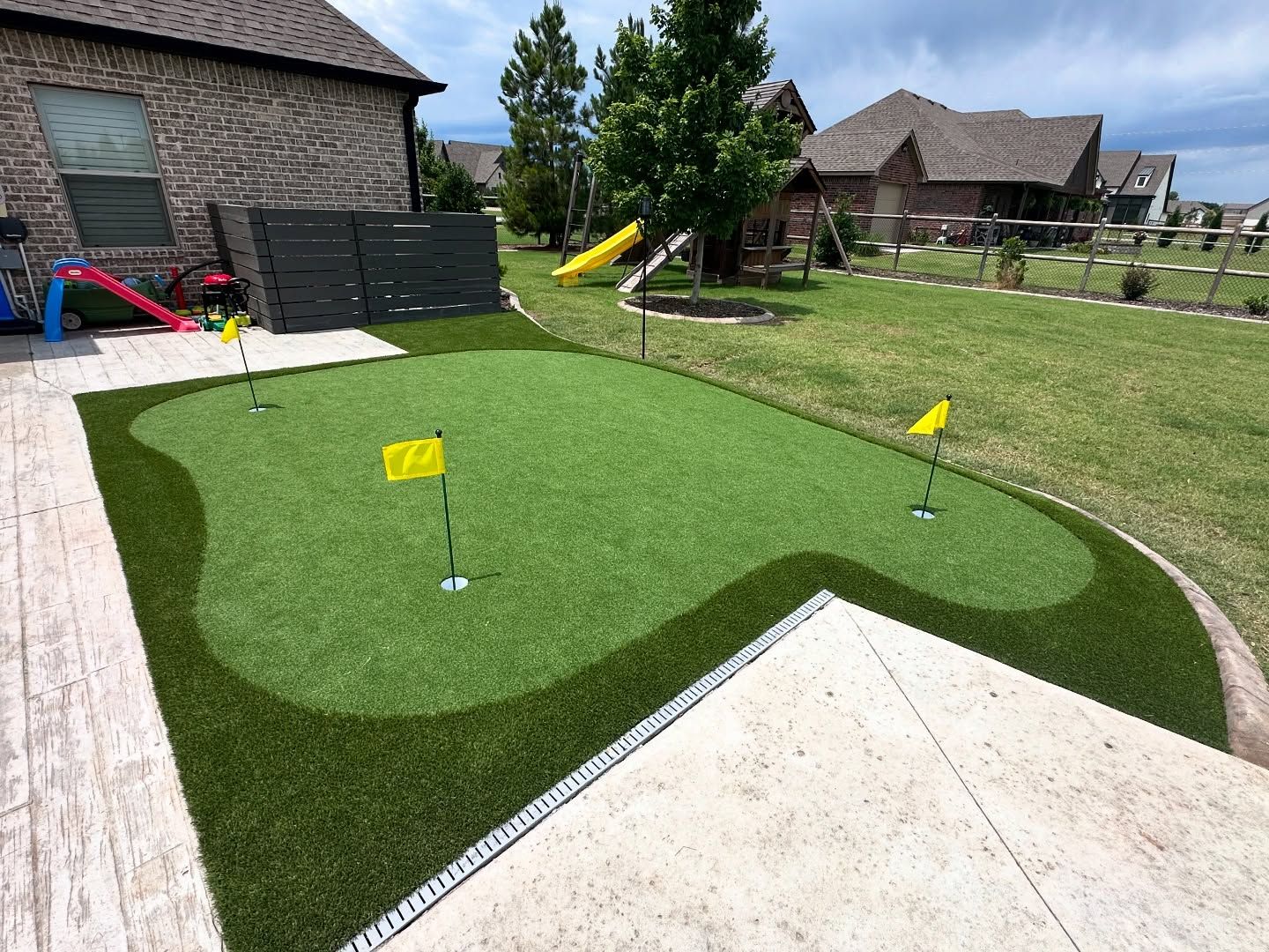 Backyard putting green with yellow flags, adjacent patio and playground.