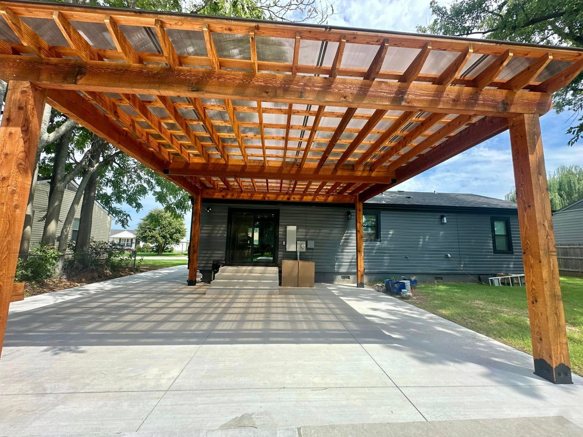 Wooden pergola over a concrete driveway, attached to a gray house.