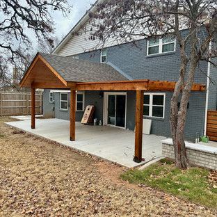 A concrete patio with a wood-framed pergola attached to a gray brick house.