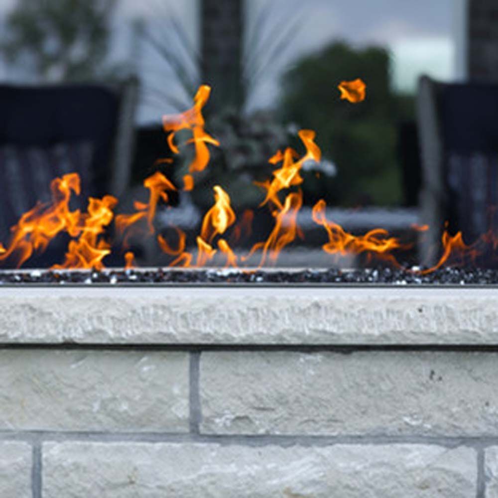 Fire pit with flickering flames against a light stone facade, with a blurred outdoor setting.