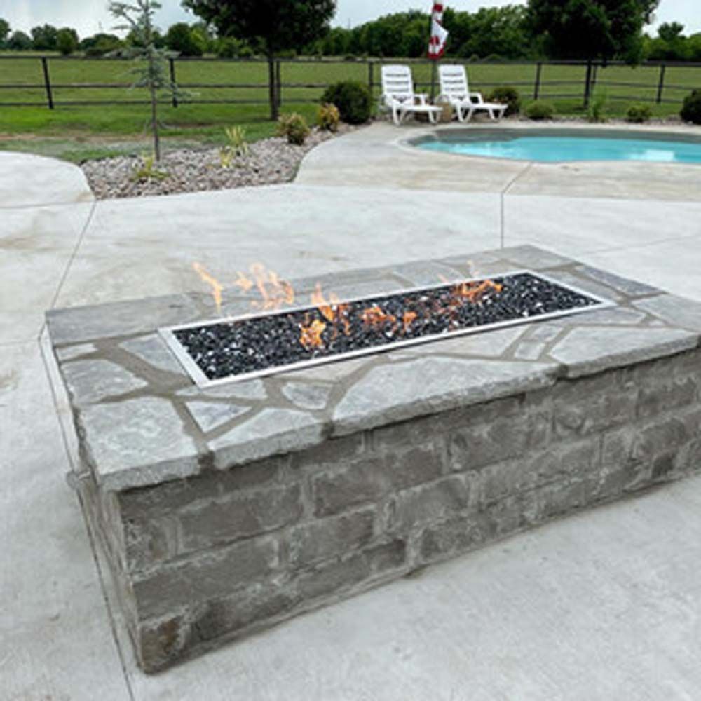 Fire pit with flames, built from stone blocks, next to a pool.