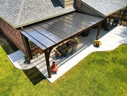 Patio with polycarbonate roof attached to a brick house, wooden support posts, and a dining table set.
